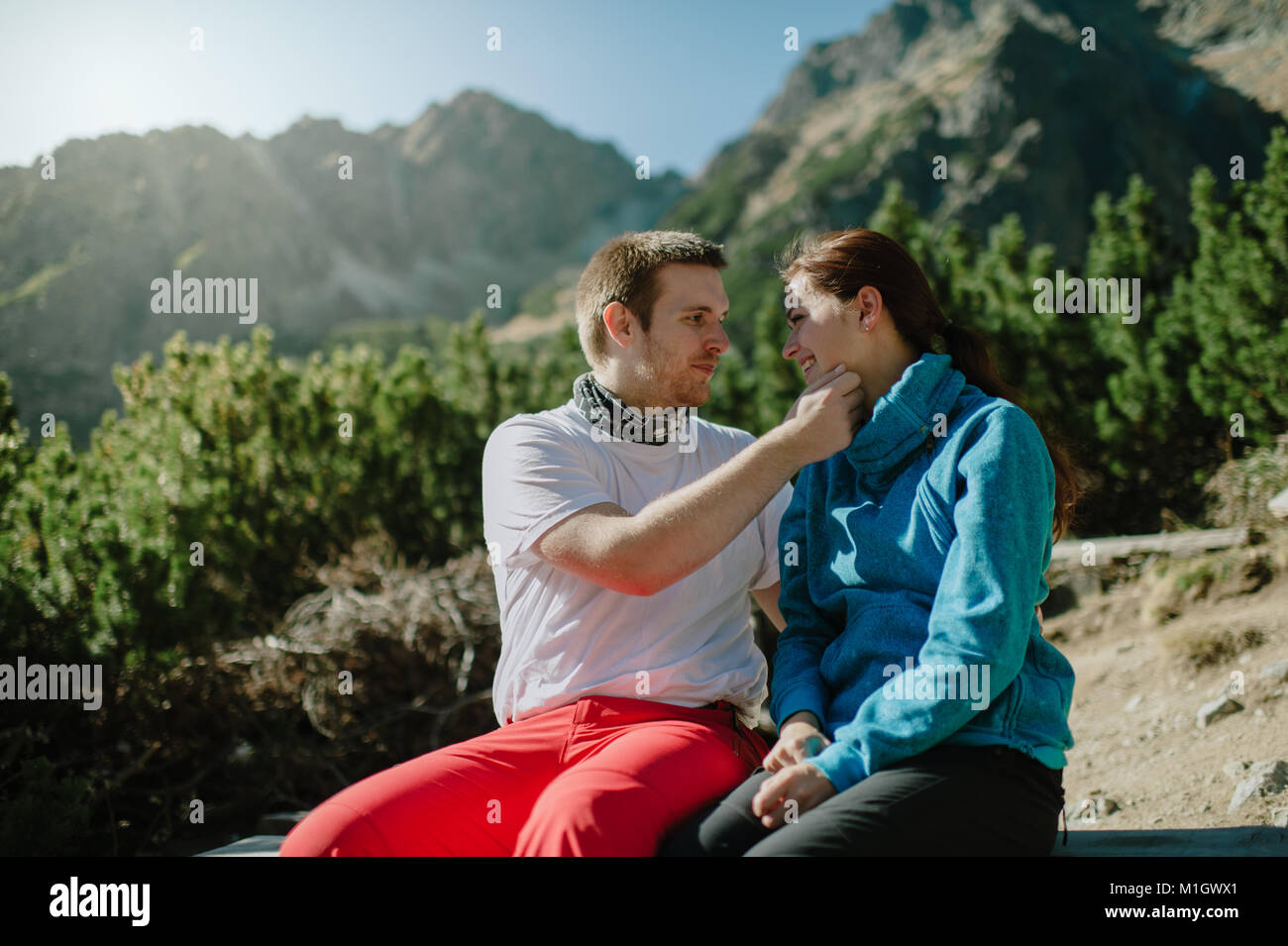 Portrait of a happy man and woman sitting o a rock with a mountain ...