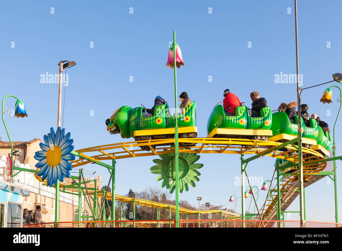 Parents and young children on a Wacky Worm Roller Coaster  at a seasonal winter funfair in Castello, Venice, Italy showing the track against a blue sk Stock Photo