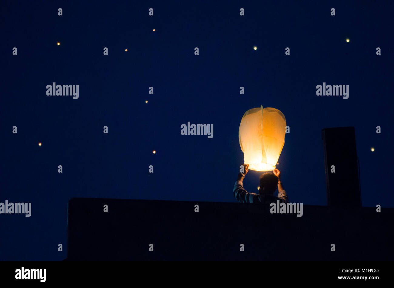 Silhouette of man flying paper sky lantern shot against a sky filled