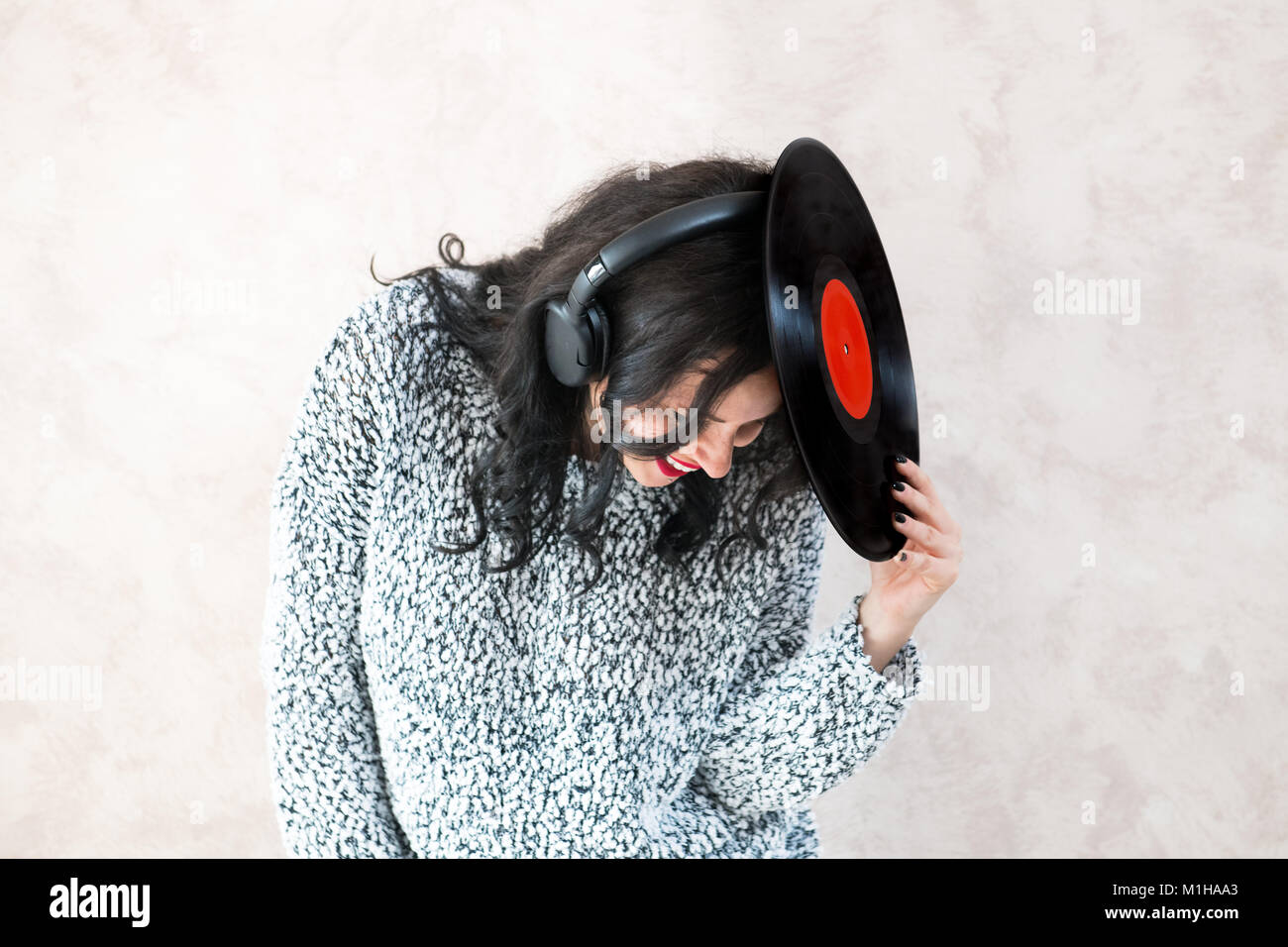 Young brunette pretty woman with vintage vinyl record on her head smiling while listening music Stock Photo