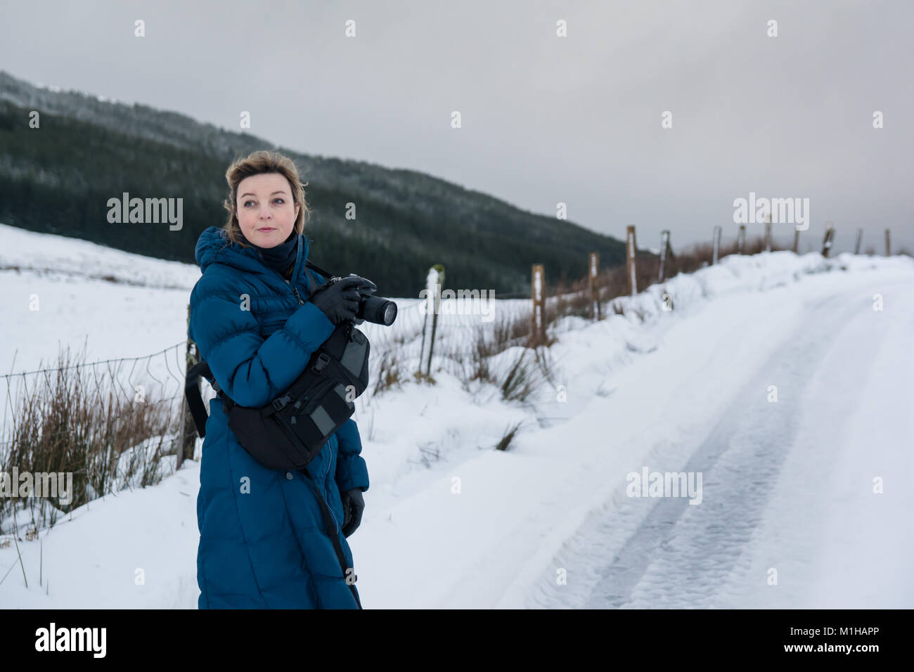 Female photographer in a blue coat taking landscape pictures in the snow in winter Stock Photo