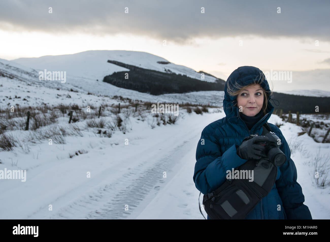 Female photographer in a blue coat taking landscape pictures in the snow in winter Stock Photo