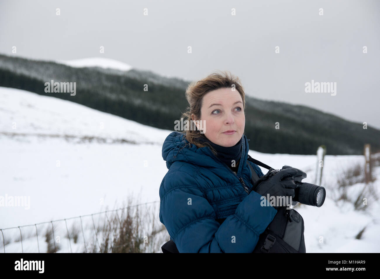 Female photographer in a blue coat taking landscape pictures in the snow in winter Stock Photo