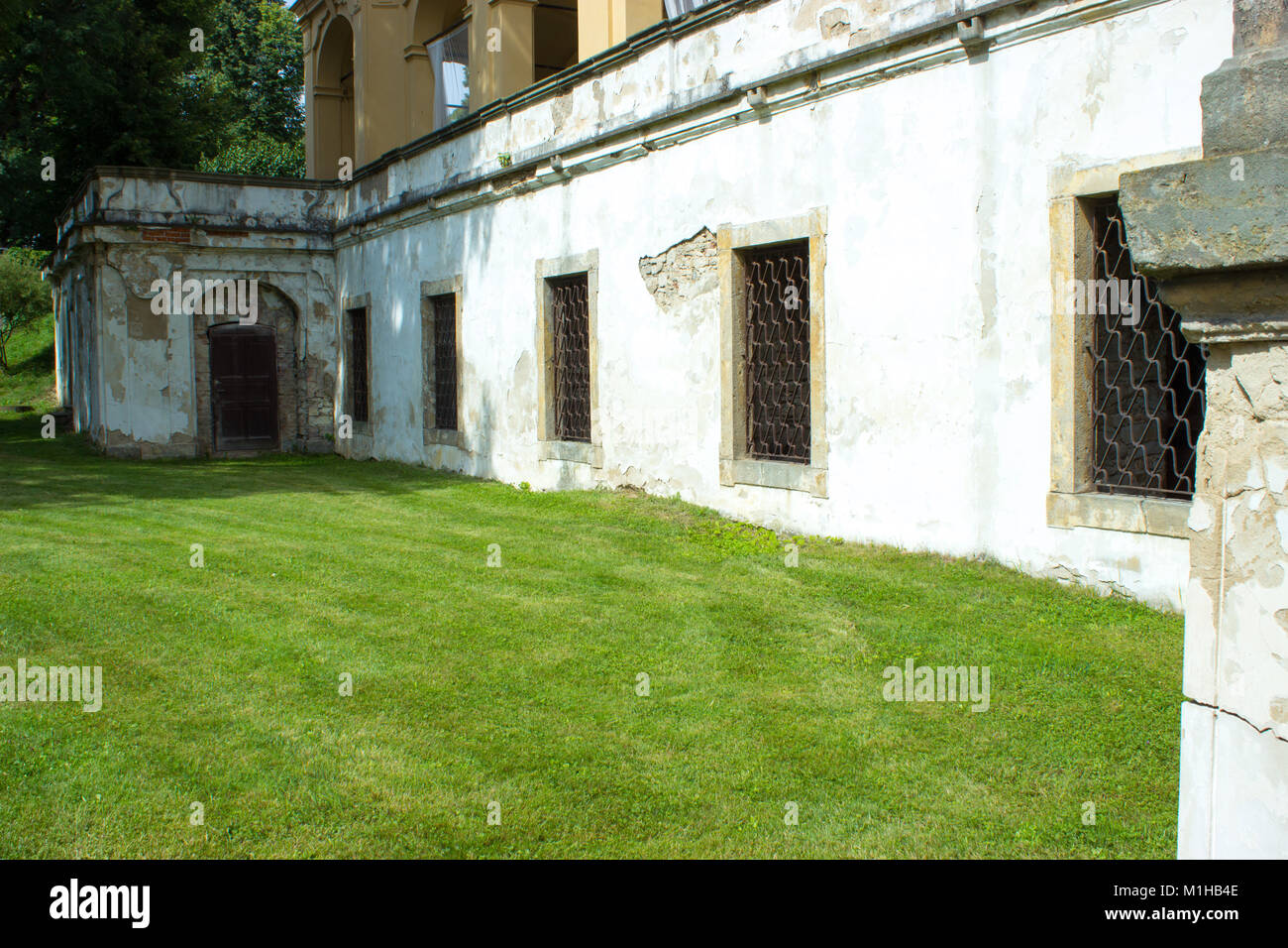 View of old flaked walls and barred windows of the building. The lawn is cut in the foreground. Stock Photo
