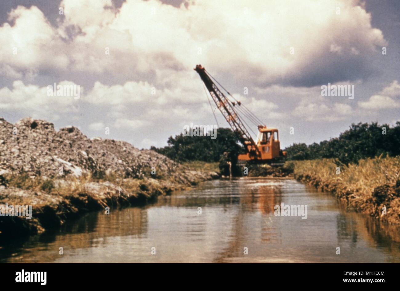 A dragline excavator clearing debris from a drainage canal to prevent the influx of vector-borne diseases and flood damage, 1976. Image courtesy CDC. () Stock Photo