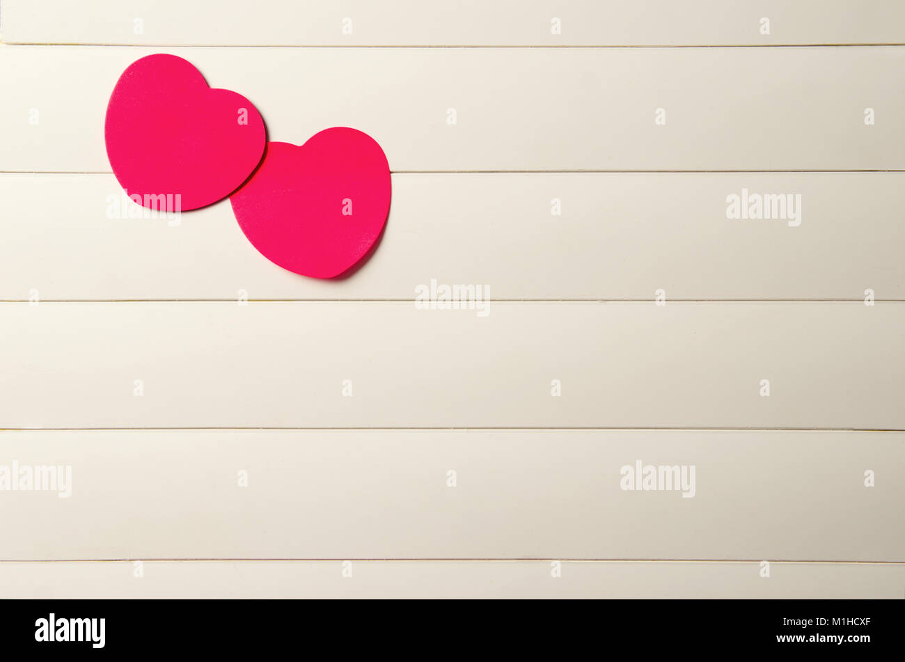 two red paper hearts on a light striped background. there is a space ...