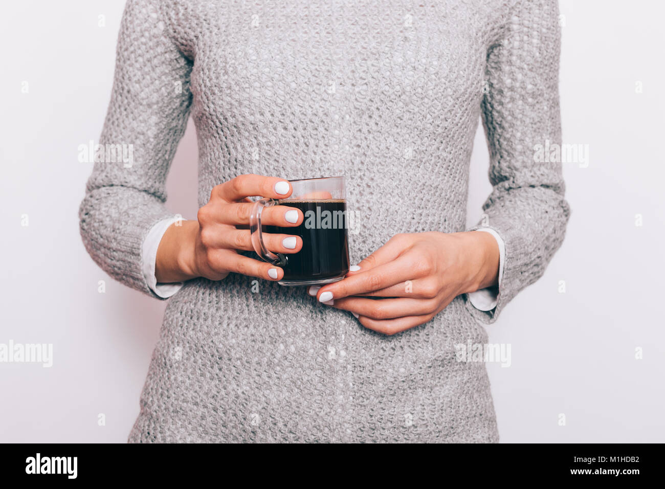 Cropped image of a slender woman in a shirt and sweater holding a cup ...