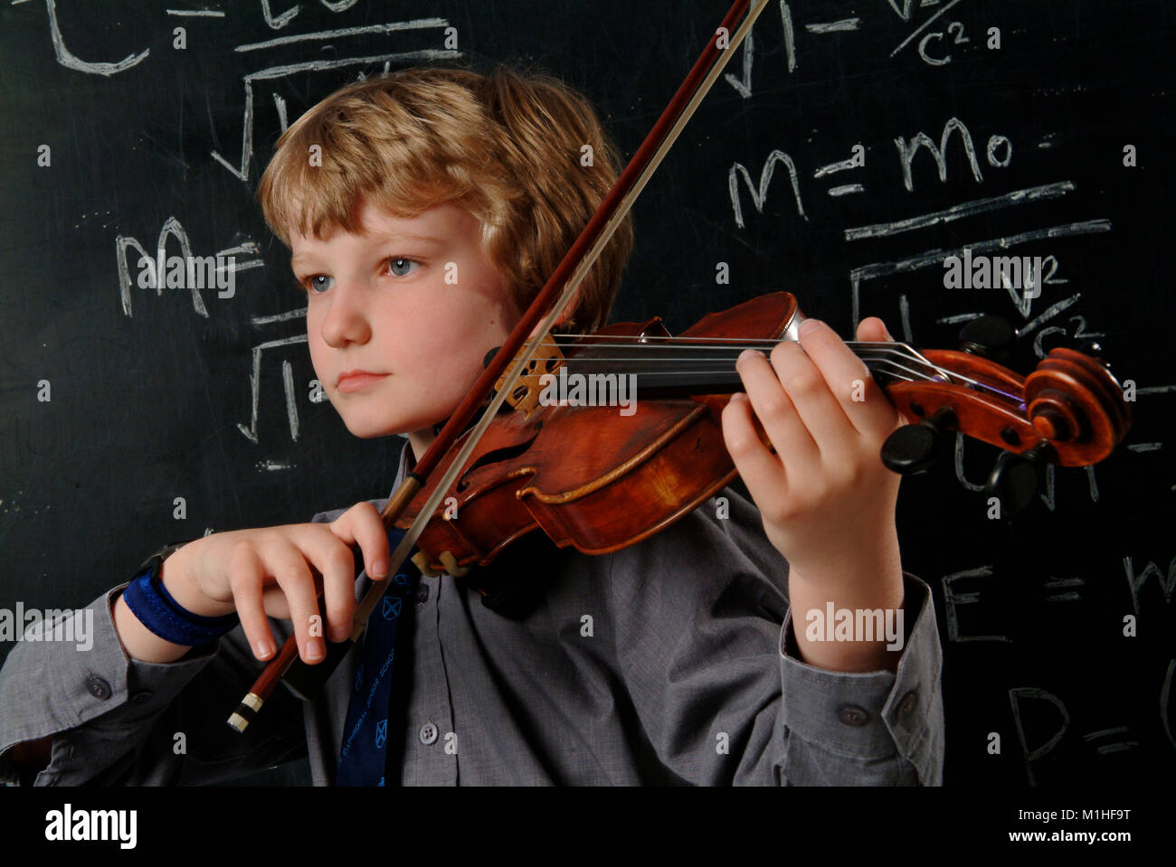 A young male school student who is an accomplished violin player and mathematician, seen in front of a blackboard, equasion and Albert Einstein photo Stock Photo