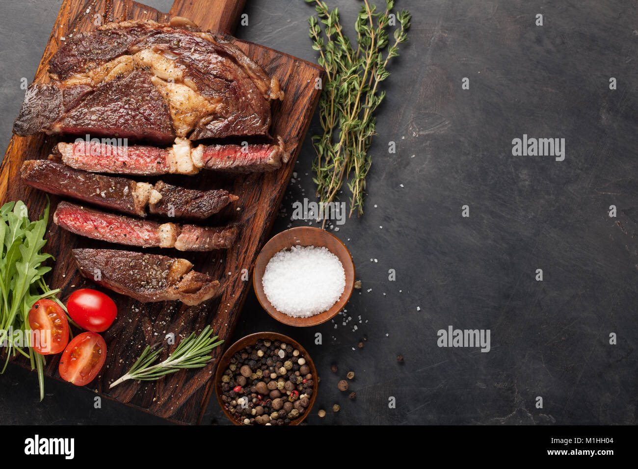 Grilled ribeye beef steak with red wine, herbs and spices on a dark ...