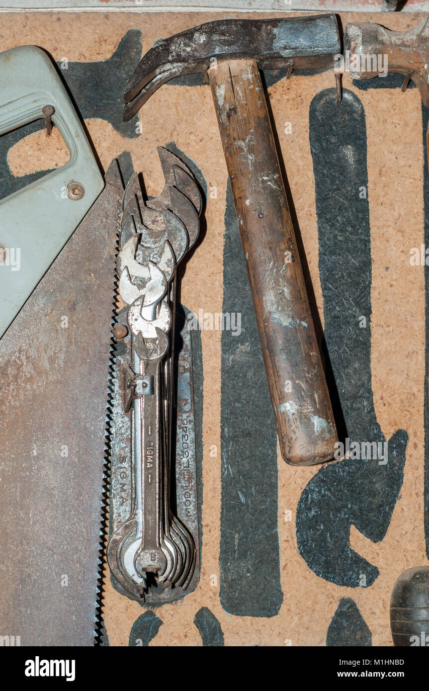 old spanners, hammer and saw placed on a wooden wall with marks with