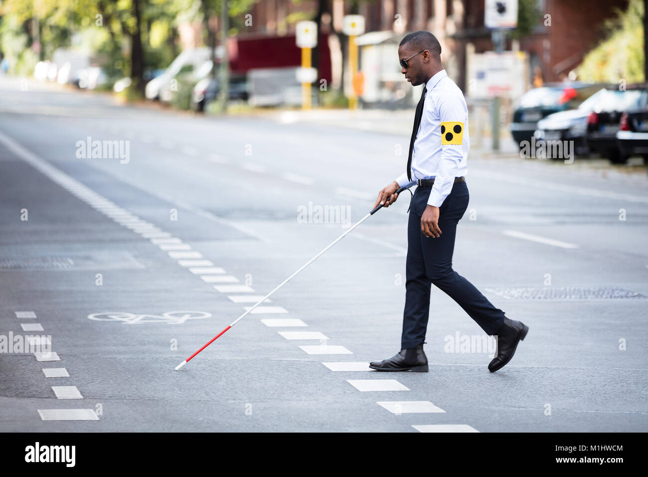 Young African Blind Man Wearing Armband Walking With Stick Crossing Road Stock Photo