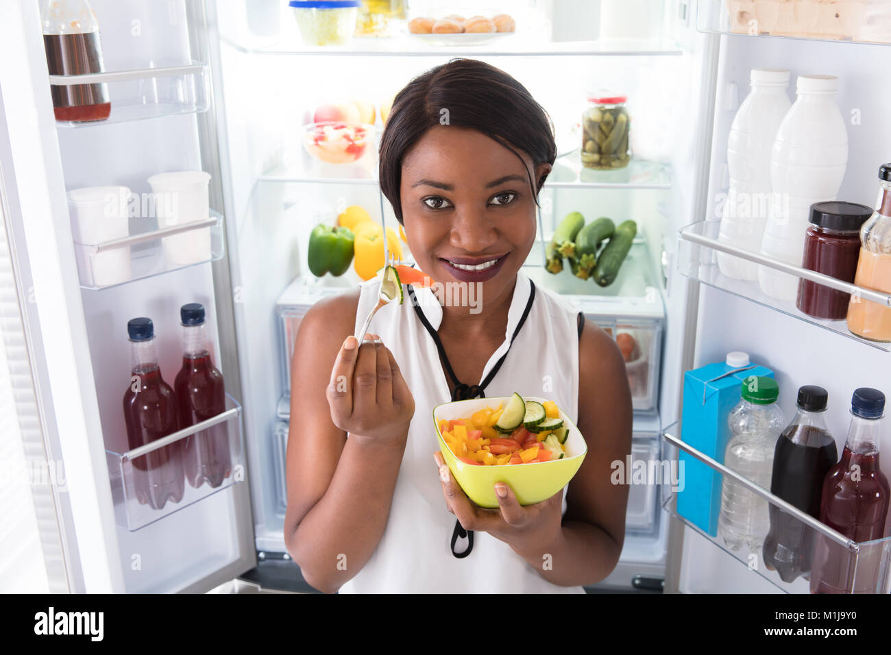 Portrait Of A Happy Young African Woman Eating Fruits In Bowl Stock Photo
