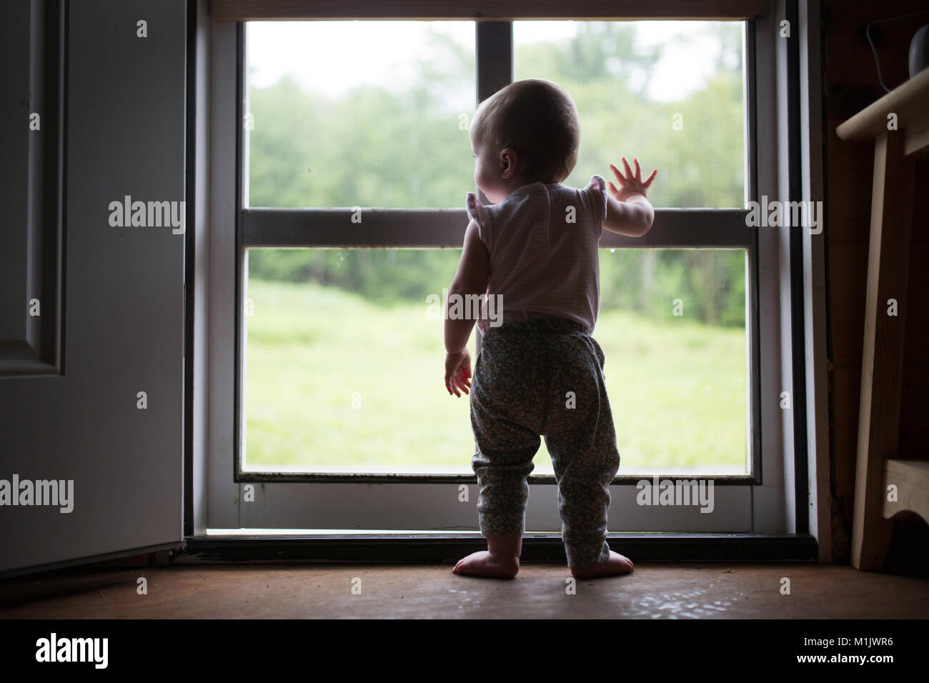 Rear View of Infant Child Standing at Screen Door Stock Photo