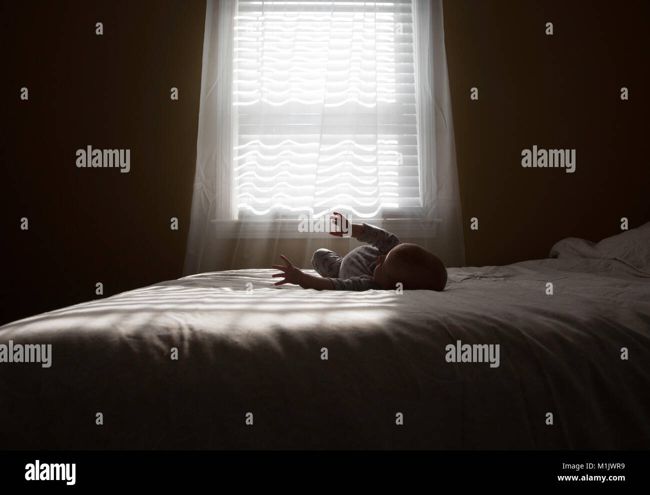 Baby Laying on Bed in front of Window Stock Photo