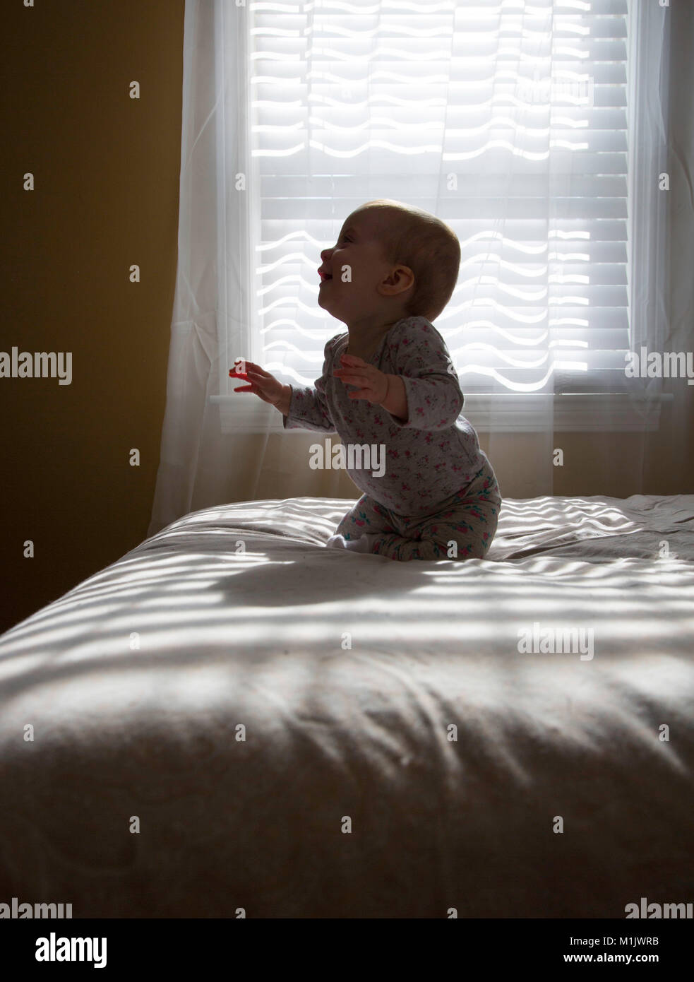Profile of Laughing Baby Kneeling on Bed Stock Photo