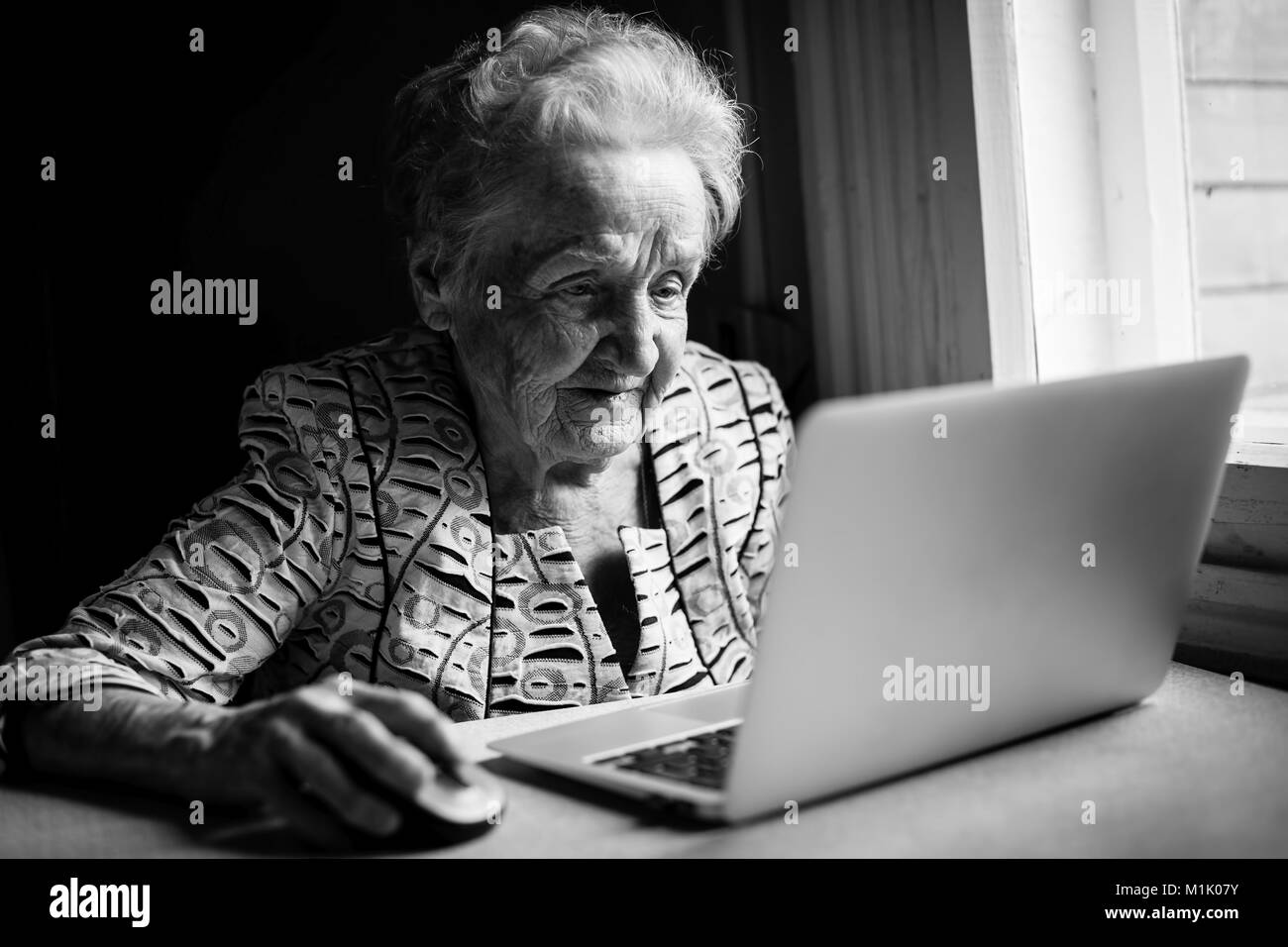 An elderly woman works on a laptop. Black-and-white photograph. Stock Photo