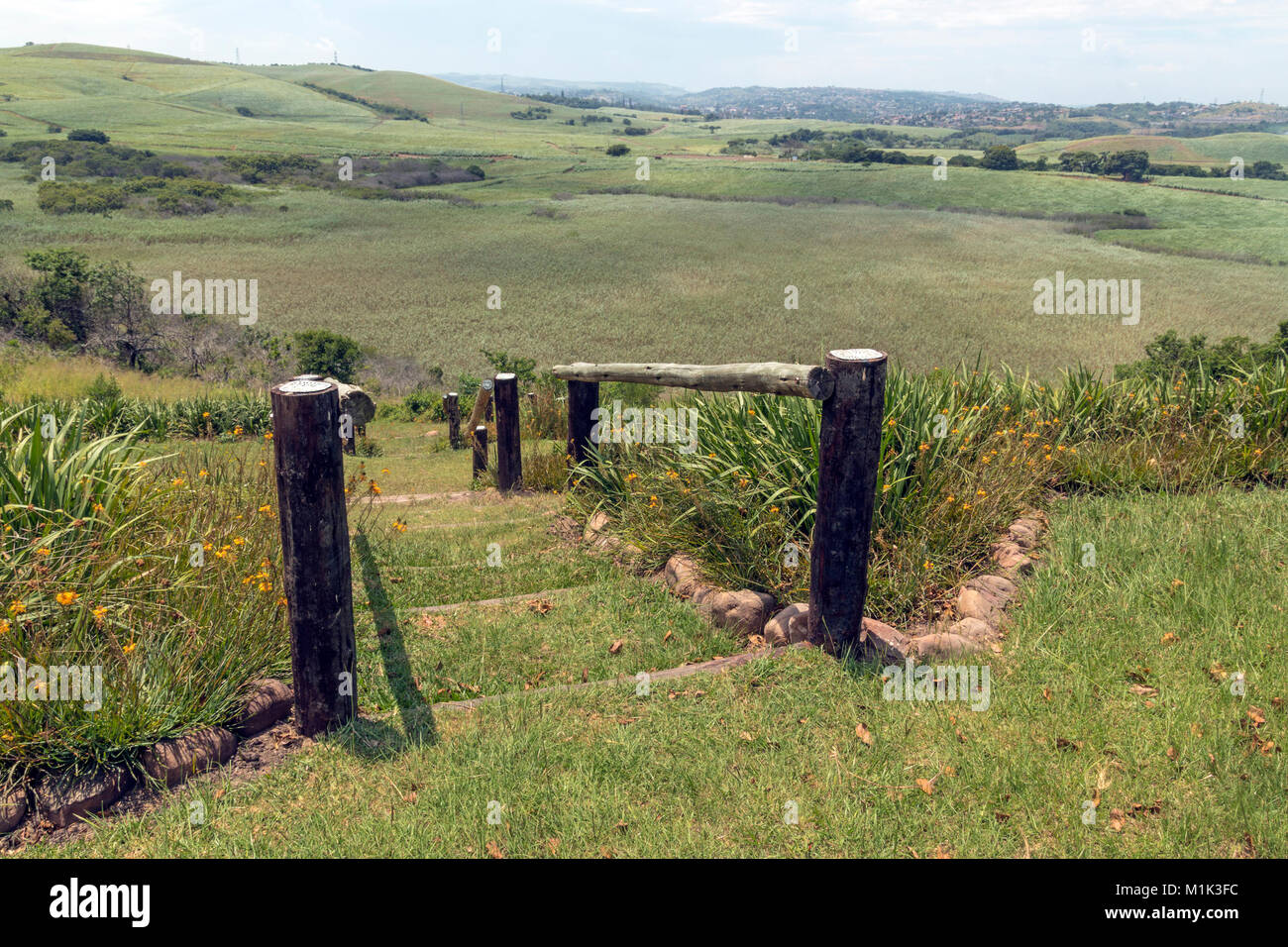 Wooden pole barrier fenced walkway , green vegetation and sugar cane plantations against distant Durban blue cloudy  skyline at Mount Moreland Stock Photo