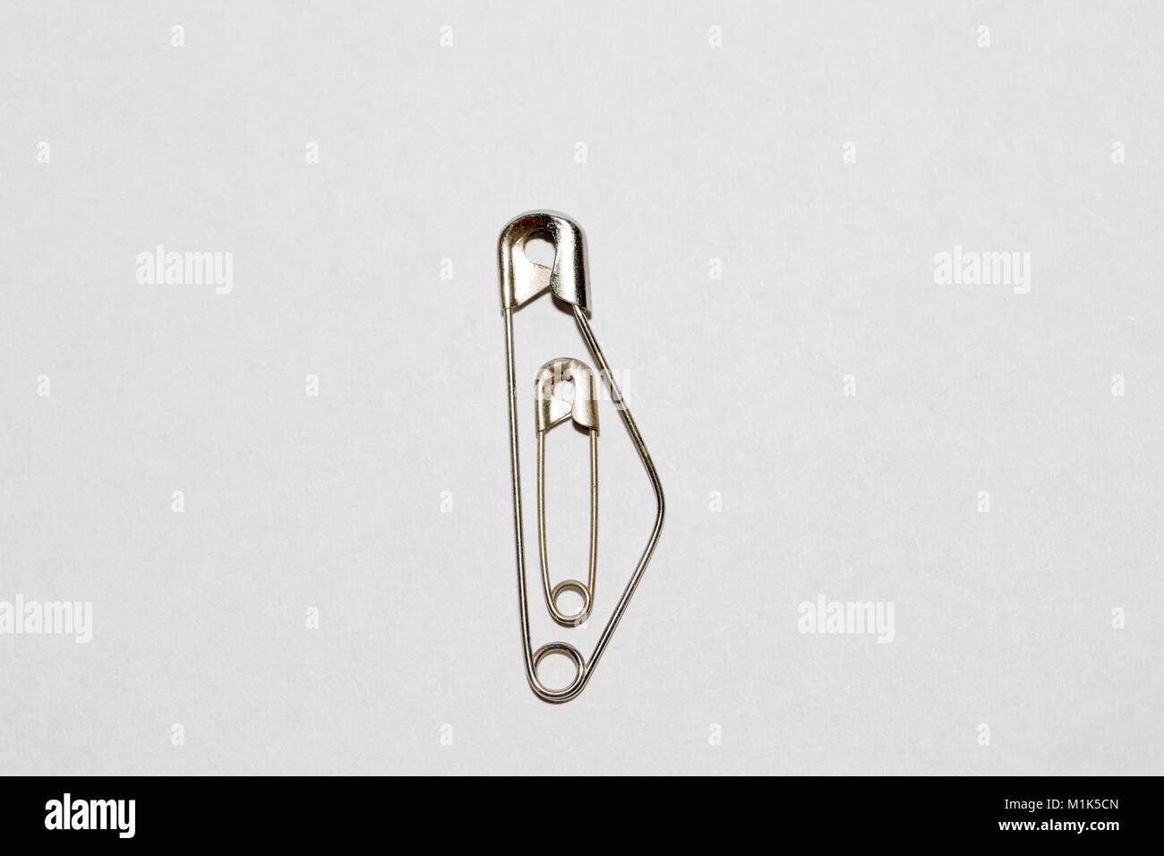 Small safety pin in a large safety pin, symbol image for safe pregnancy, cutout Stock Photo