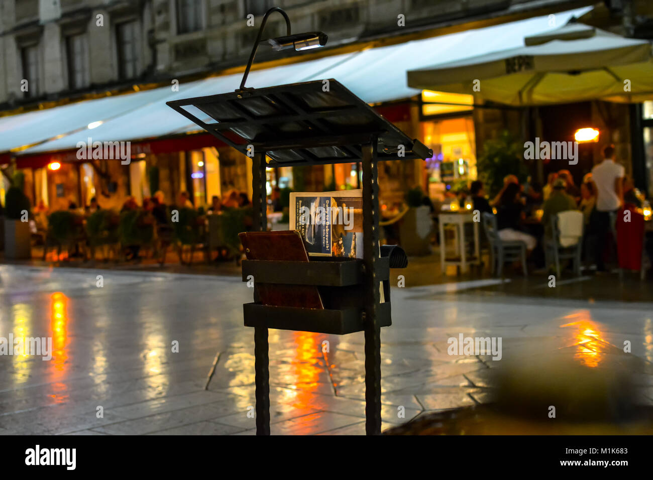 A lighted menu stand advertises a sidewalk cafe late night in Peoples Square in Split Croatia as diners enjoy a meail Stock Photo