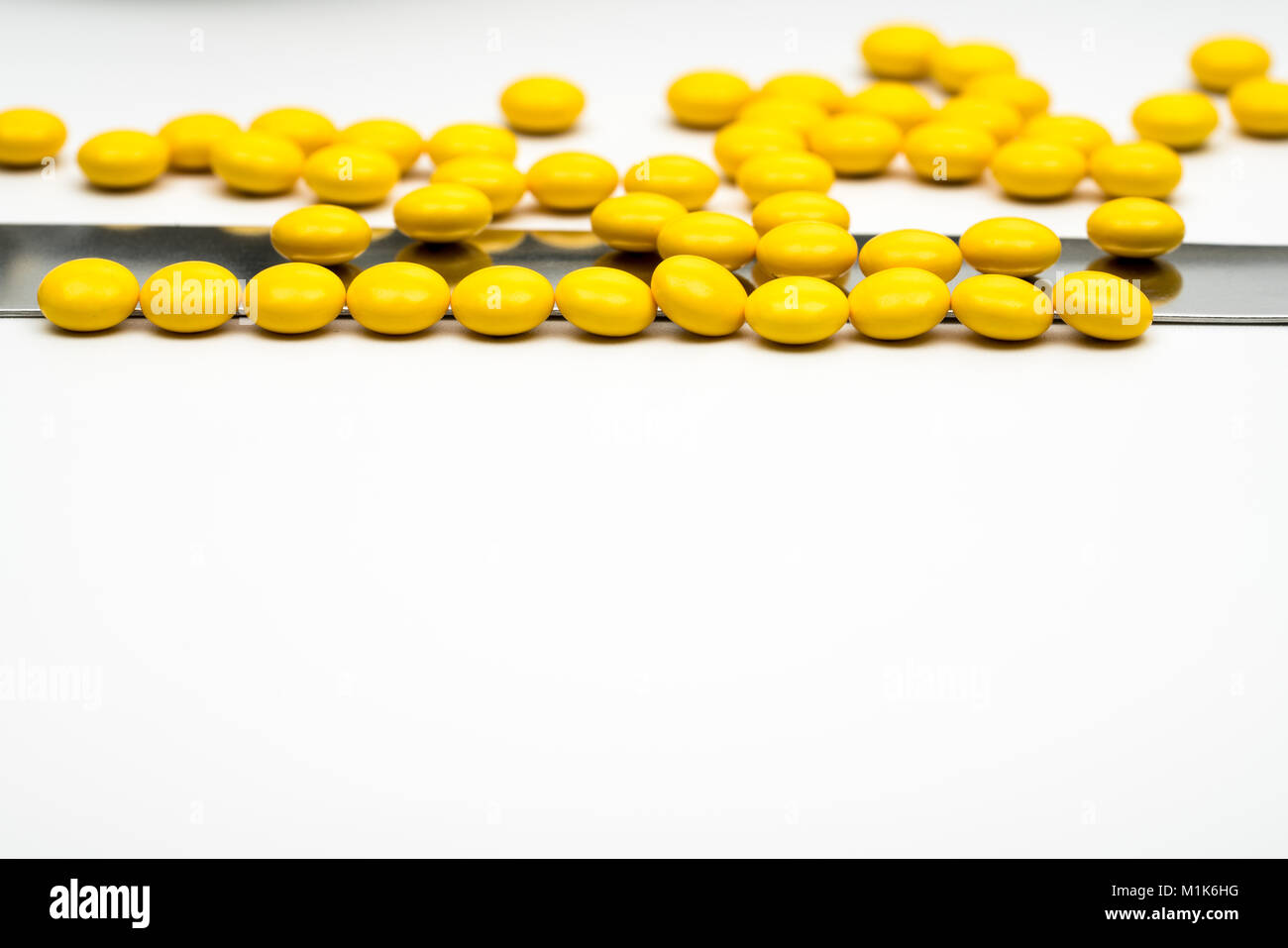 Macro shot detail of yellow round sugar coated tablets pills and stainless steel spatula on white background with copy space Stock Photo