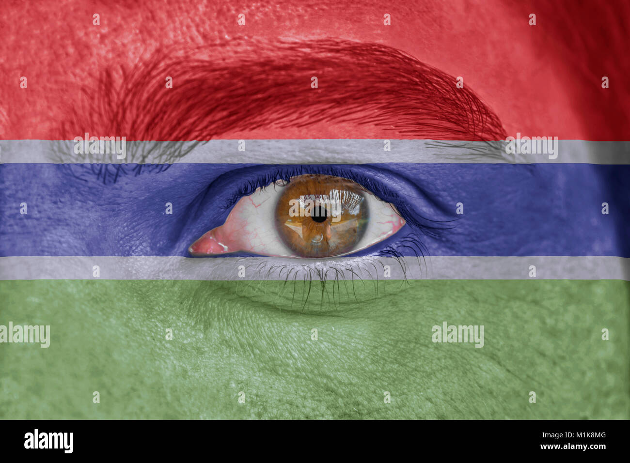 Human face and eye painted with flag of Gambia Stock Photo