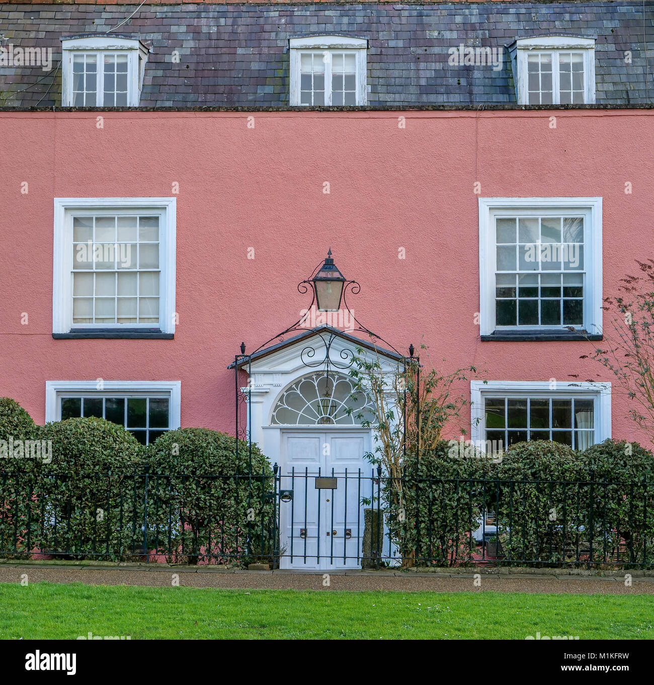 Pink painted Georgian house with wrought iron arched gate with lamp on Cathedral Green in Wells Somerset UK Stock Photo