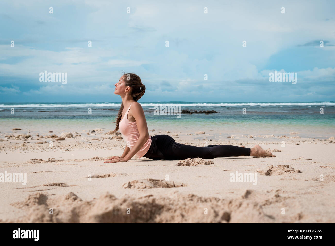 Young woman practicing yoga cobra pose on the beach near the ocean at sunrise Stock Photo