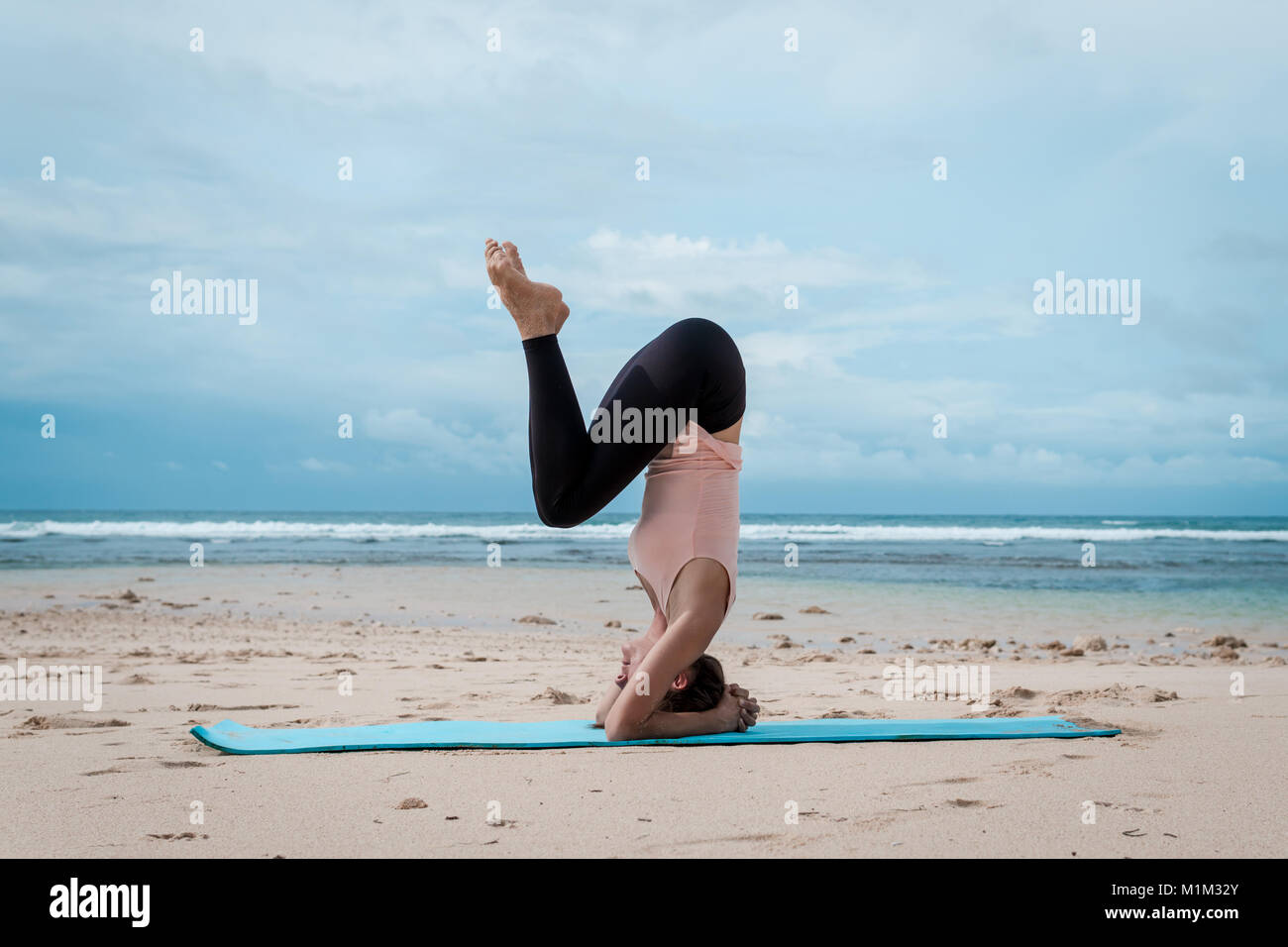 Young woman practice balance asanas on Summer yoga session on beach. Headstand Stock Photo