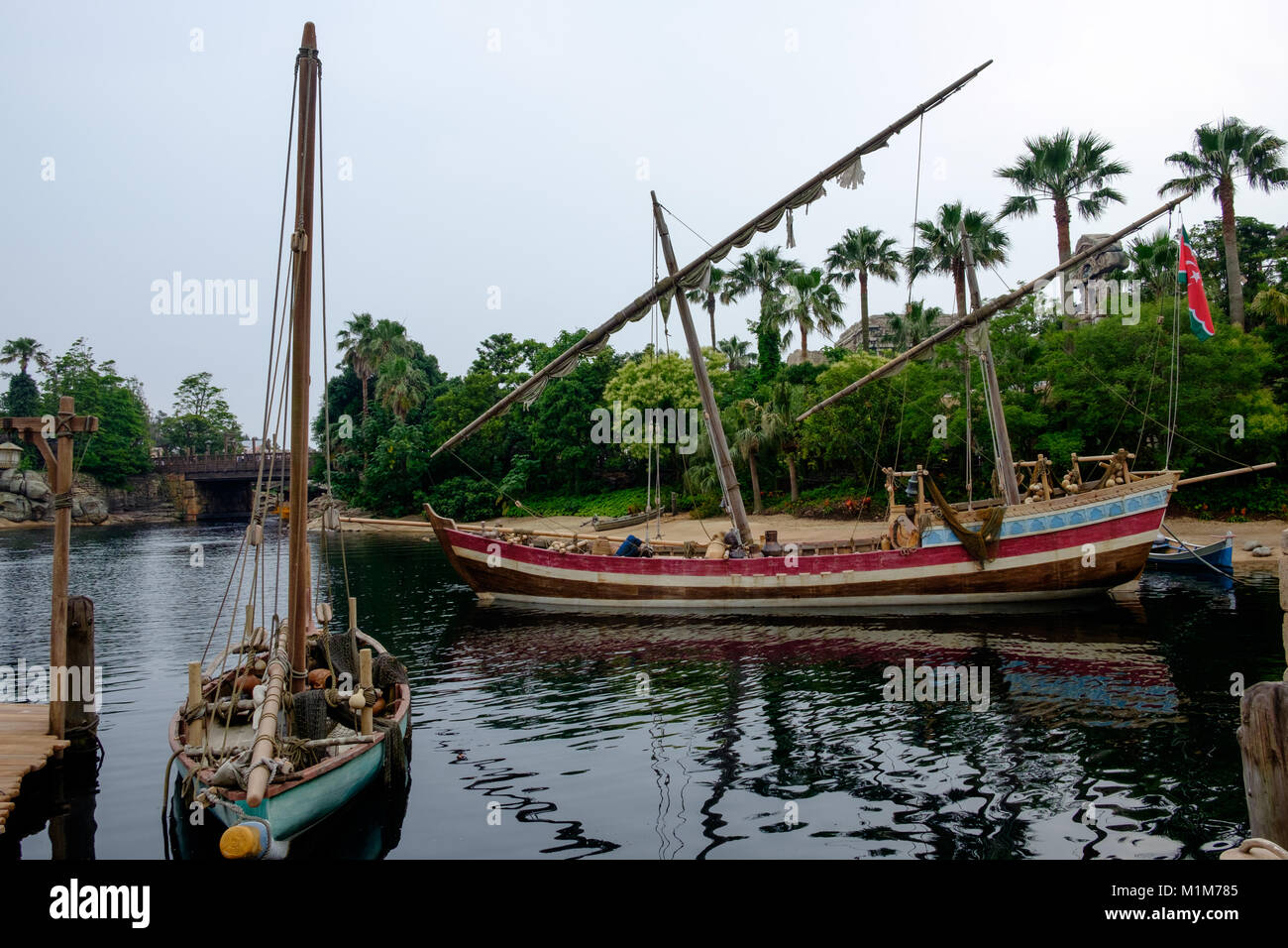 Two boats on the river with sails furled and the dock on the left. Palm trees in the background. Stock Photo