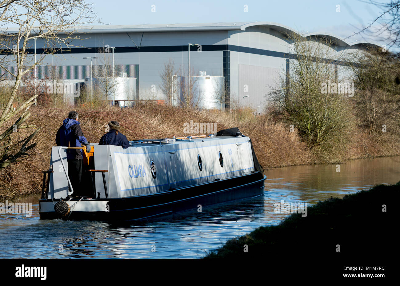 A narrowboat in winter on the Oxford Canal with warehouses behind, Banbury, Oxfordshire, England, UK Stock Photo