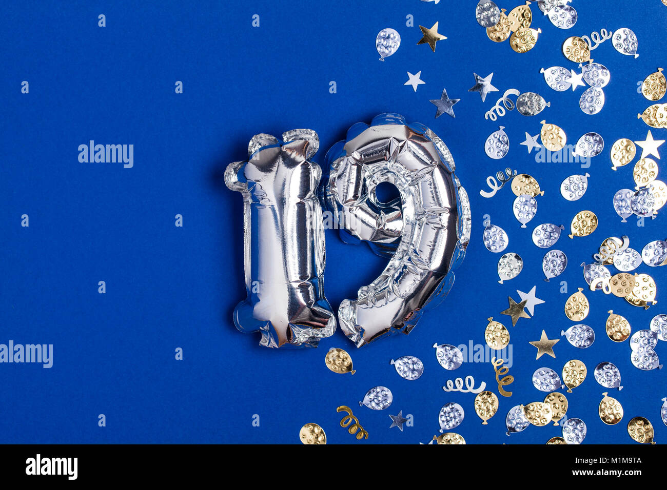 Silver foil number 19 balloon on a blue background with glitter ...