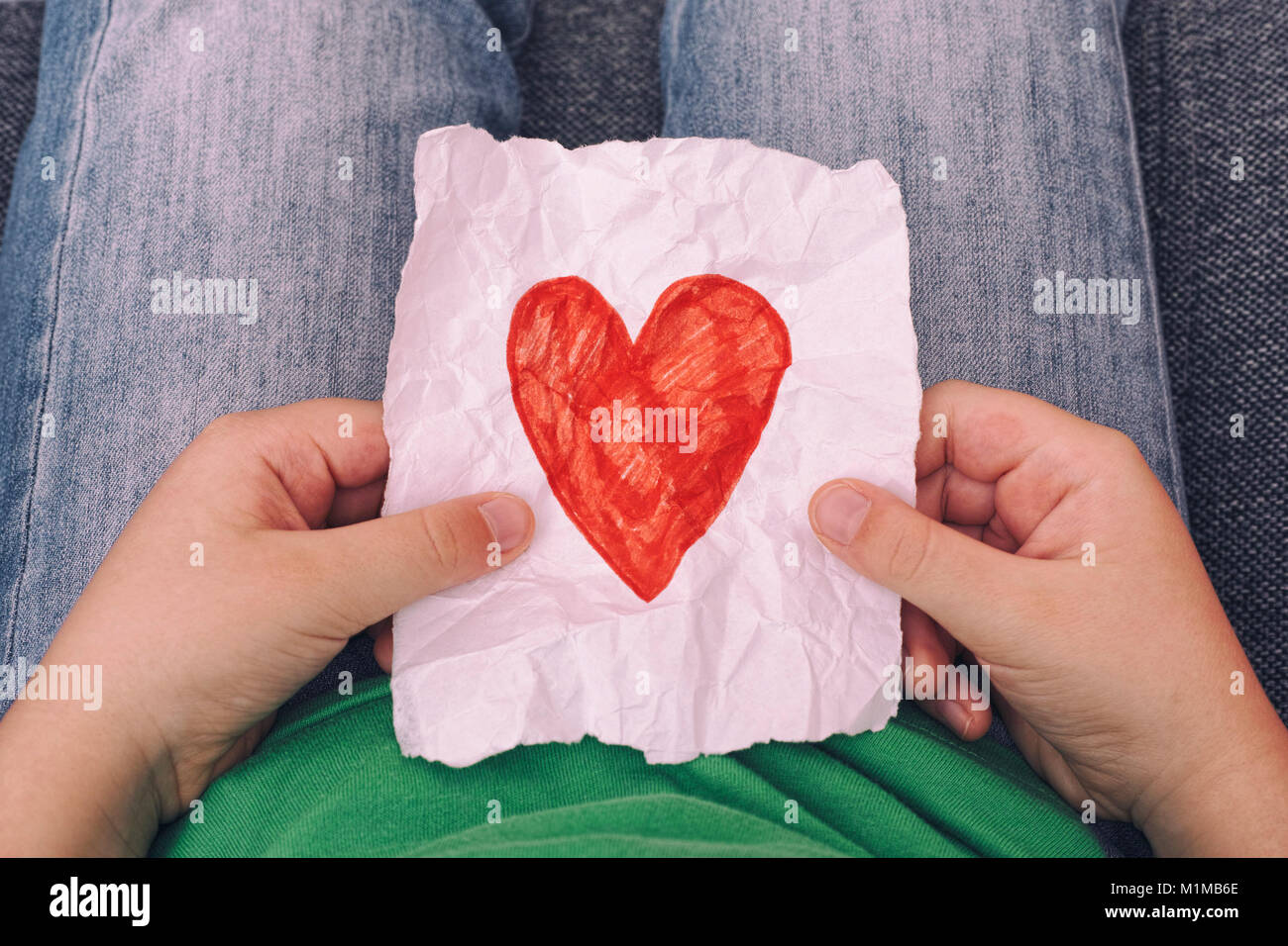 Young boy holding crumpled piece of paper with red heart shape. Close up. Stock Photo