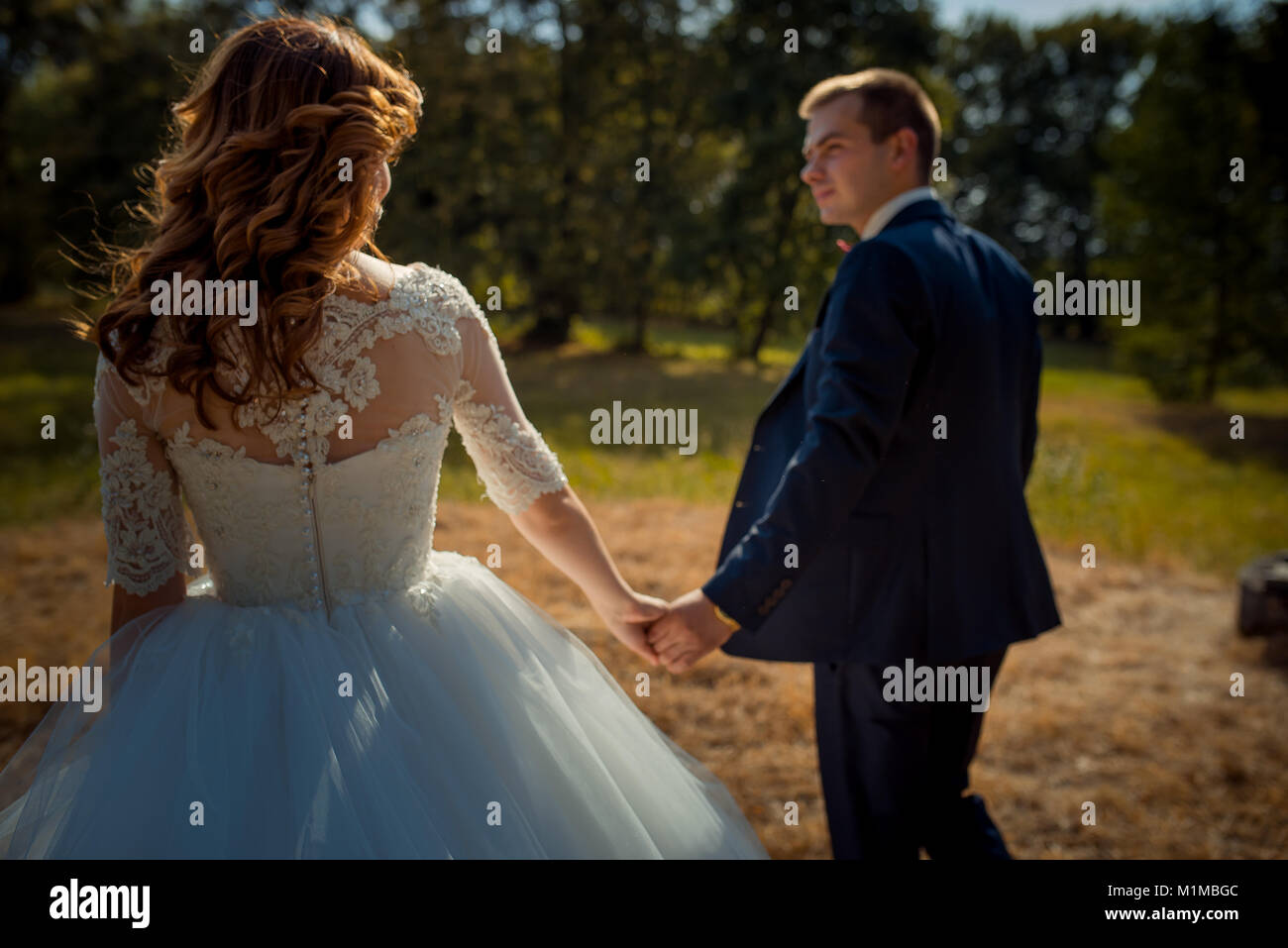Back view of the charming stylish newlyweds holding hands while walking ...