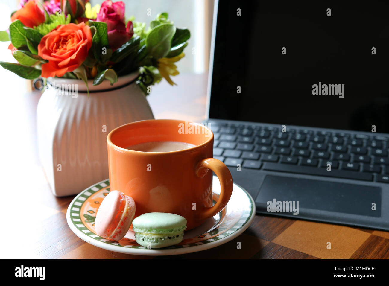 Cup of coffee with milk on the table on a foreground, the turned off computer and vase with beautiful flowers bouquet on a shallow depth of field back Stock Photo