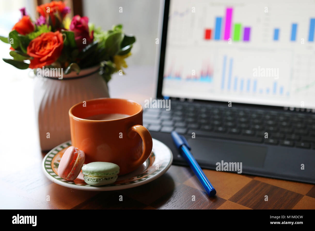 Cup of coffee with milk on the table on a foreground next to the working computer and vase with beautiful flowers bouquet on a shallow depth of field  Stock Photo