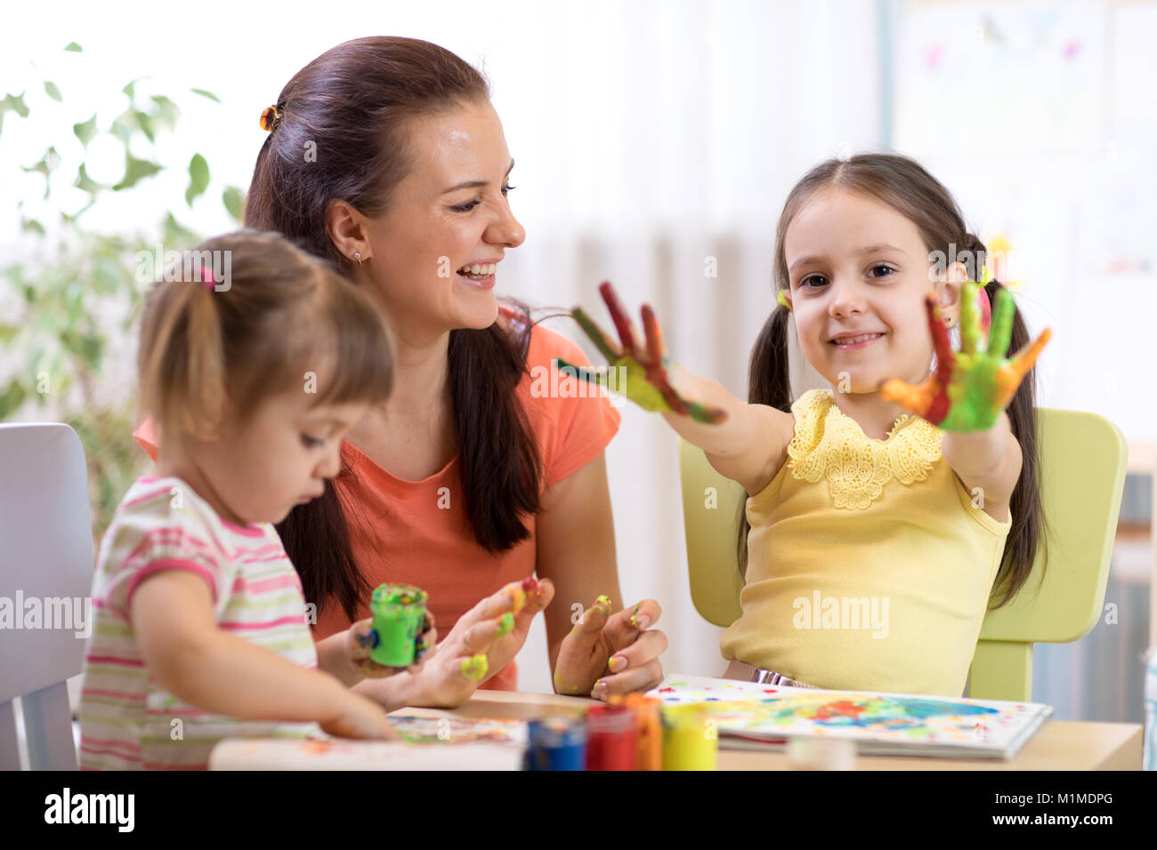 Child girl with painted hands. Kids drawing and coloring with teacher in daycare center or playschool. Stock Photo