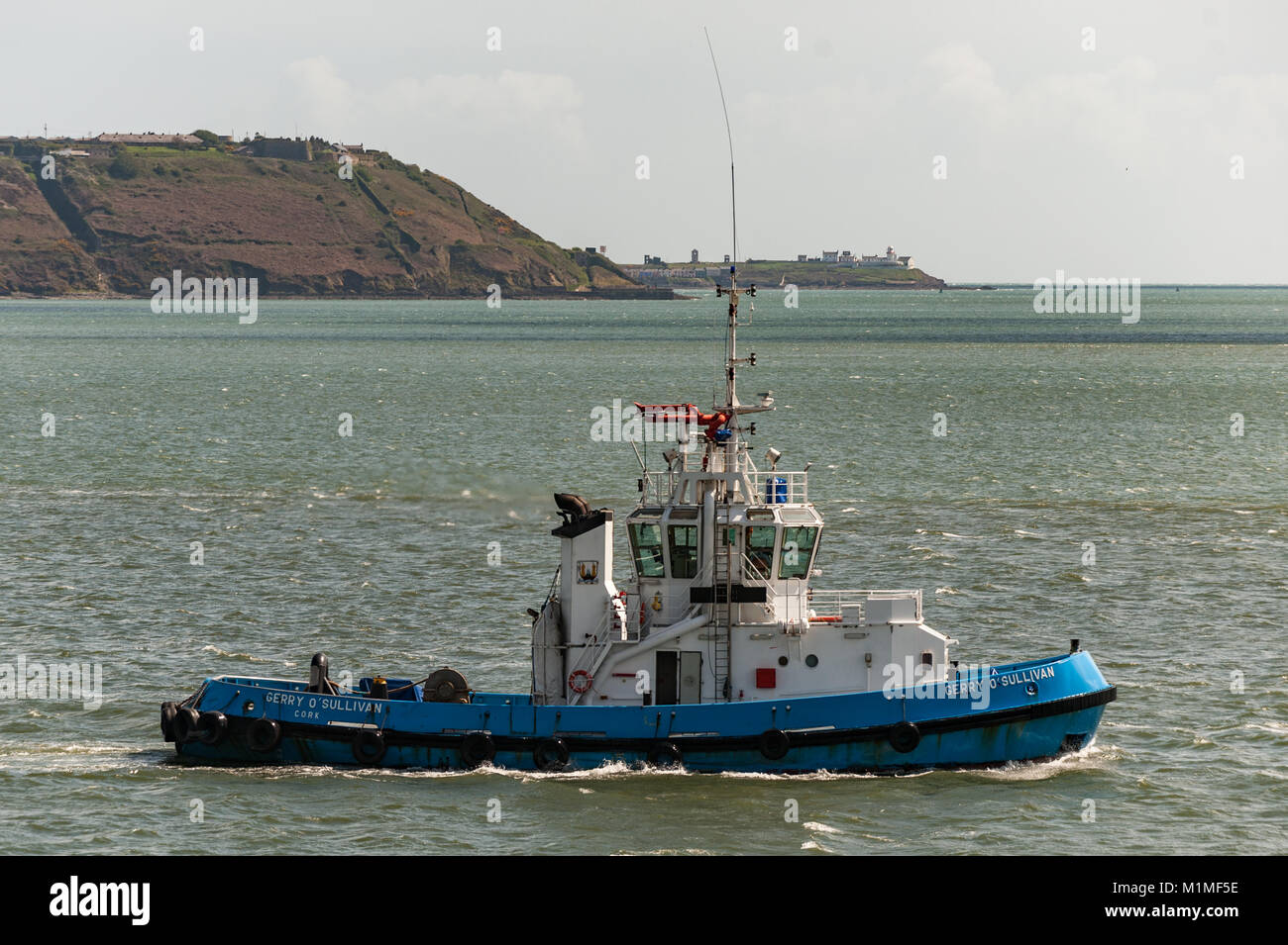 Port of Cork tugboat 'Gerry O'Sullivan' makes her way past Cobh, County Cork, Ireland with Roches Point Lighthouse in the background. Stock Photo