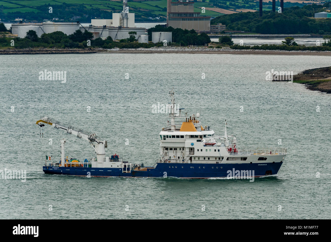 Irish Lights Ship Granuaile passes Whitegate Oil Refinery on her way out of Cork Harbour, Ireland. Stock Photo