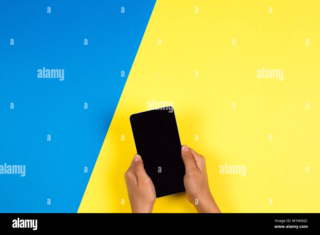 Hand holding the phone on blue and yellow background Stock Photo