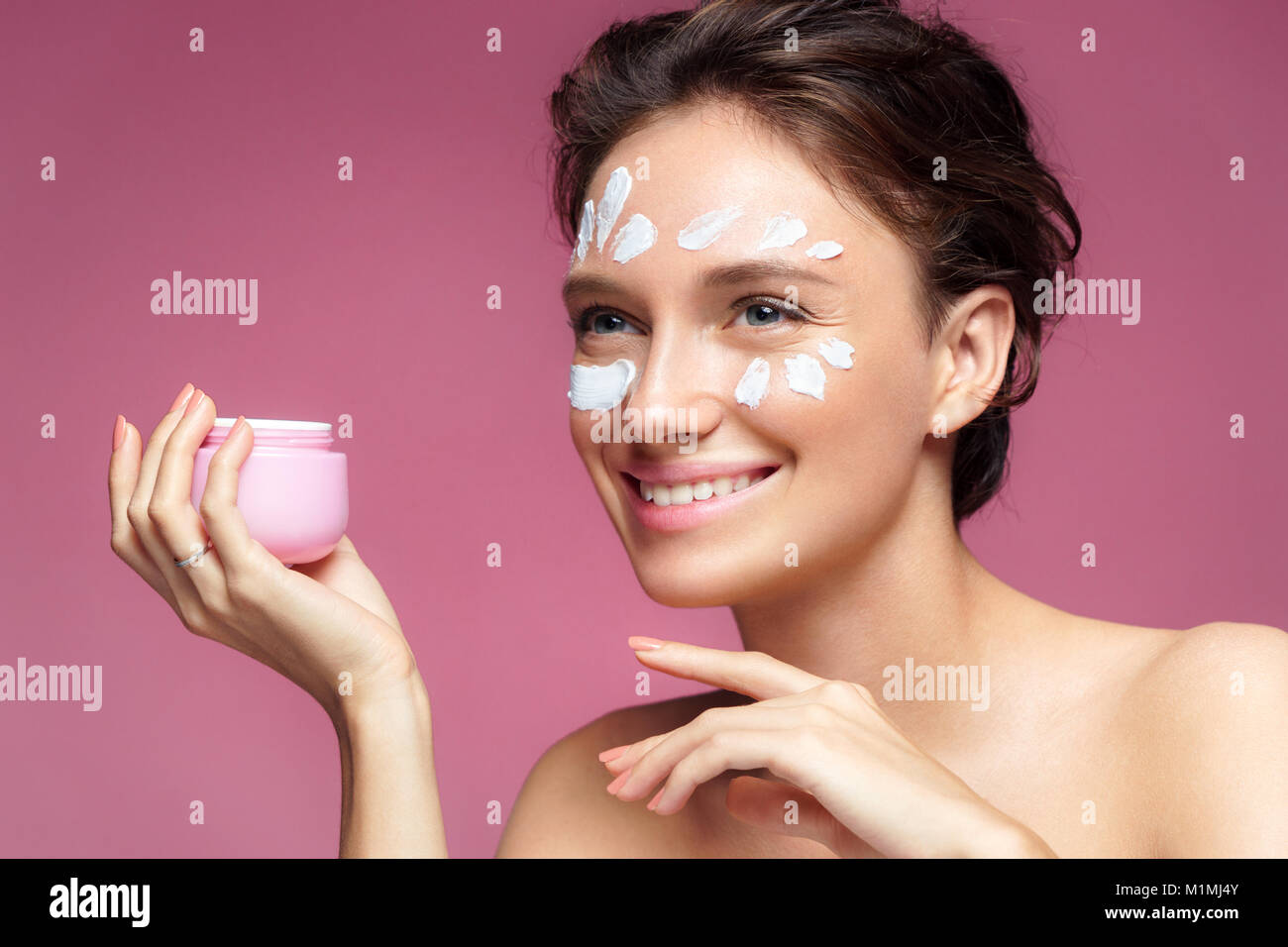 Woman applying wrinkle cream or anti-aging skin care cream. Photo of smiling woman with healthy skin on pink background. Skin care concept Stock Photo