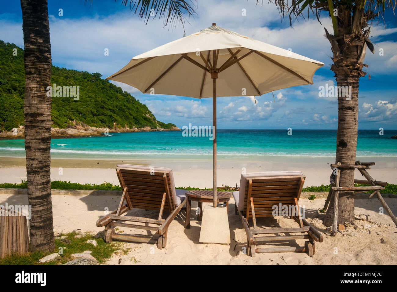 A famous tropical holiday scene with two beach chairs and an umbrella in between, flanked by palm trees. Stock Photo