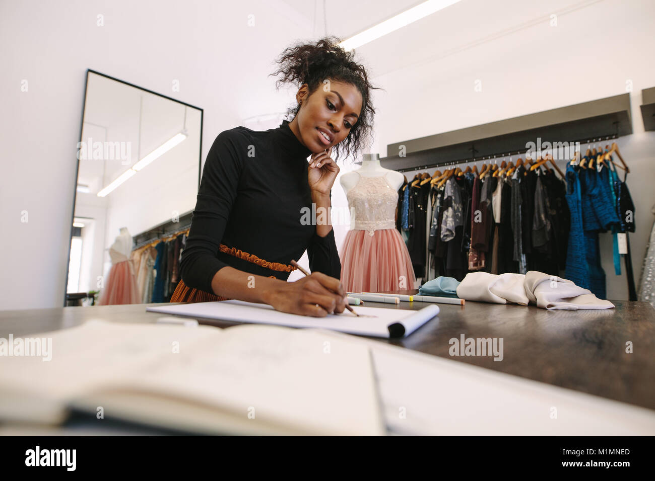 Fashion entrepreneur making a drawing at her desk. Female fashion designer sketching a design sitting in her cloth store. Stock Photo