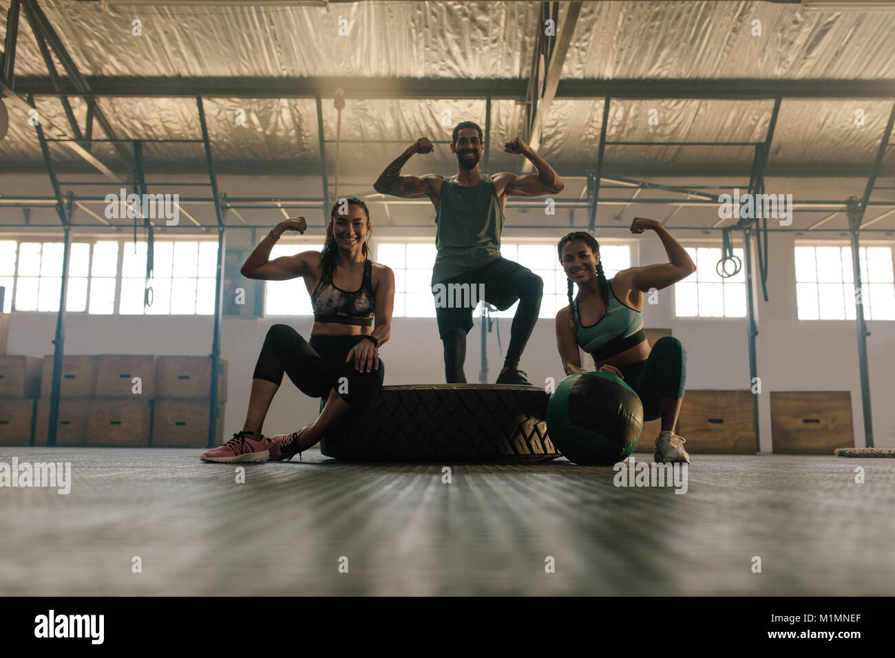 Young people posing and flexing their muscles in gym. Group of people at gym showing their muscular biceps and  smiling. Stock Photo