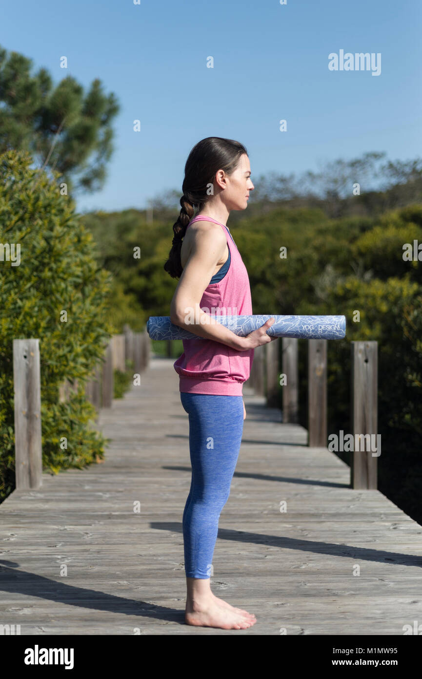 woman carrying a rolled up yoga mat, outside on a wooden deck Stock