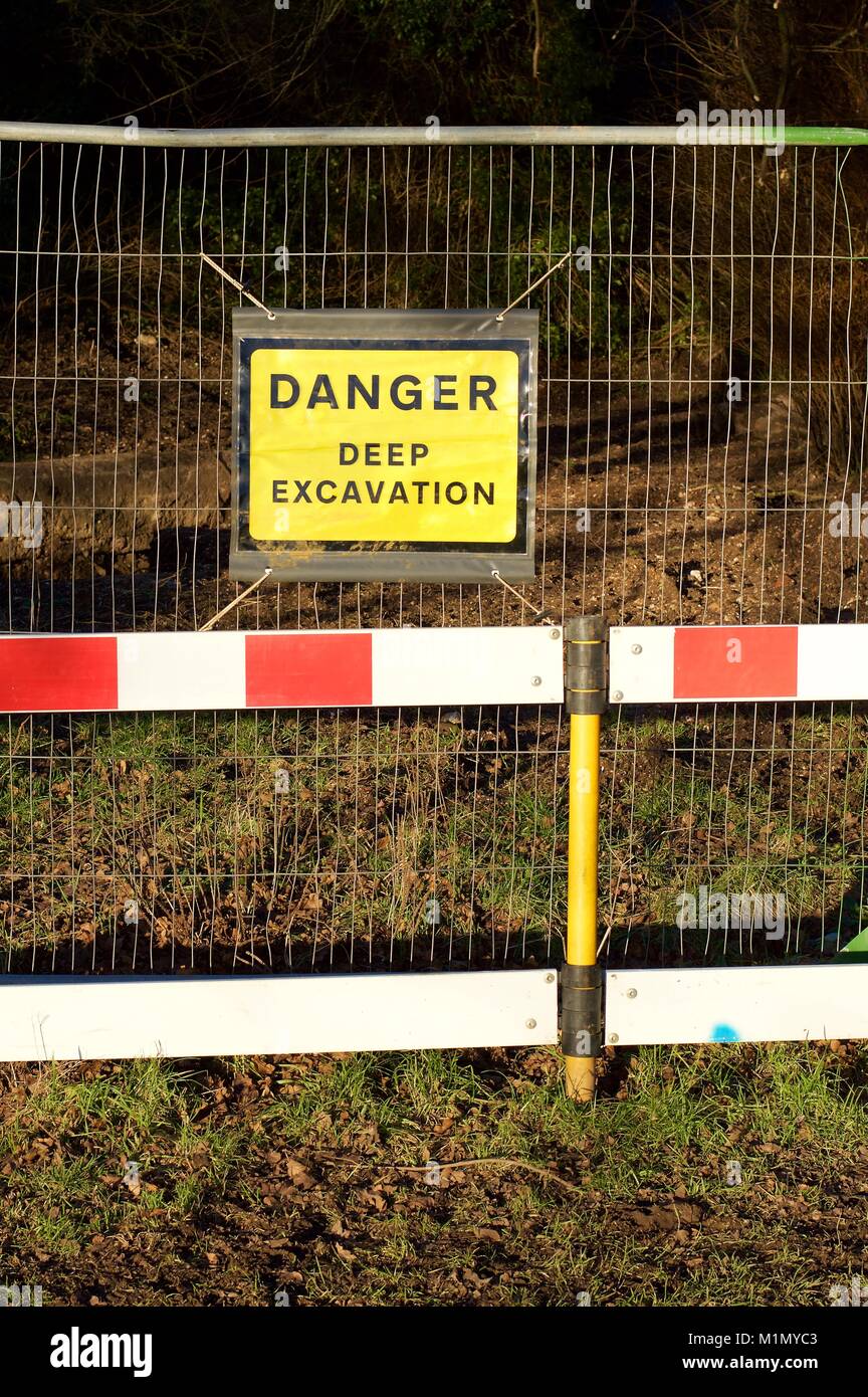 Fencing erected around a large hole during building works, with a sign reading 'Danger, deep excavation' Stock Photo