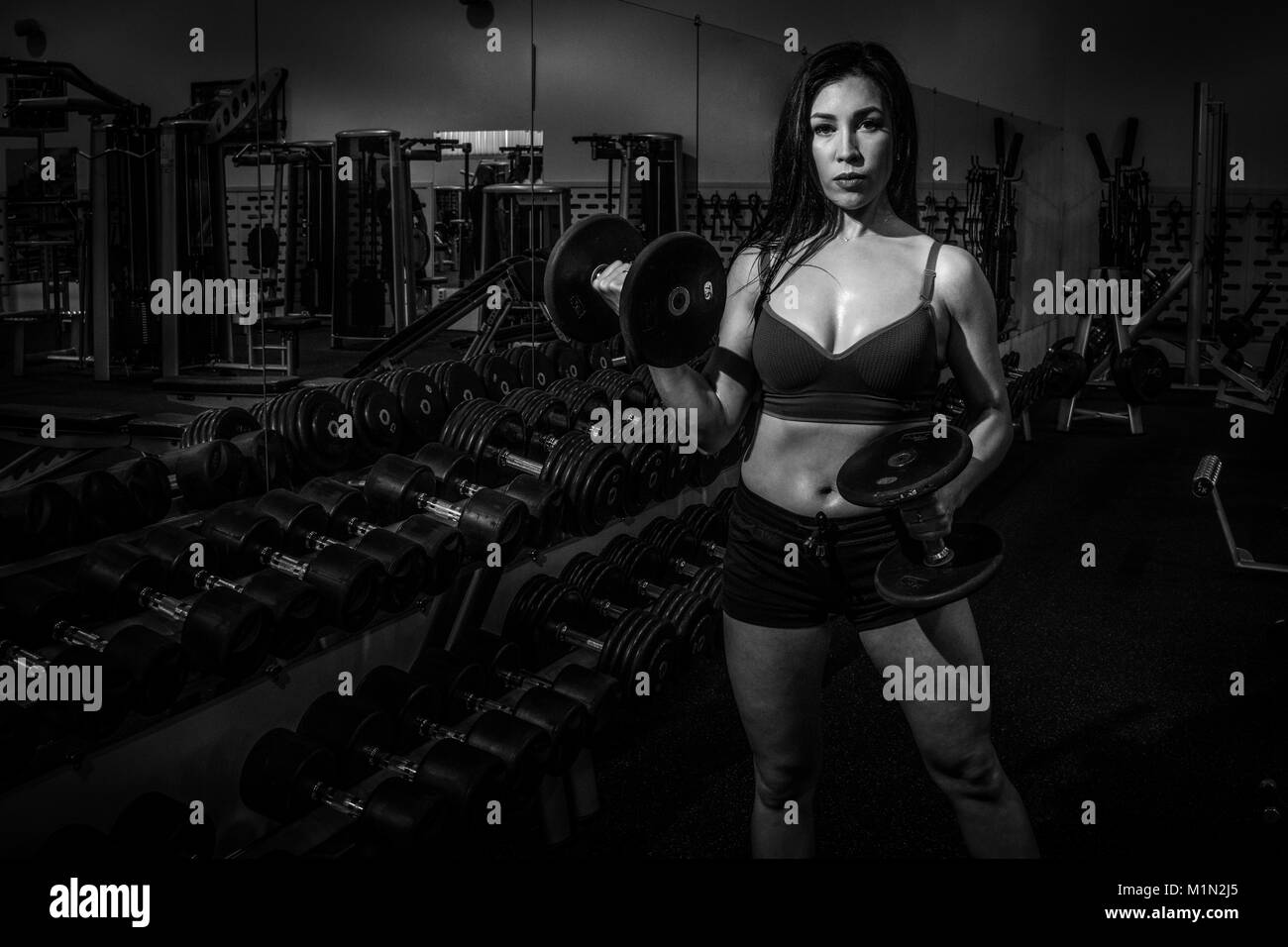 Athletic young woman in sports swimsuit raises dumbbell. Black and white Stock Photo