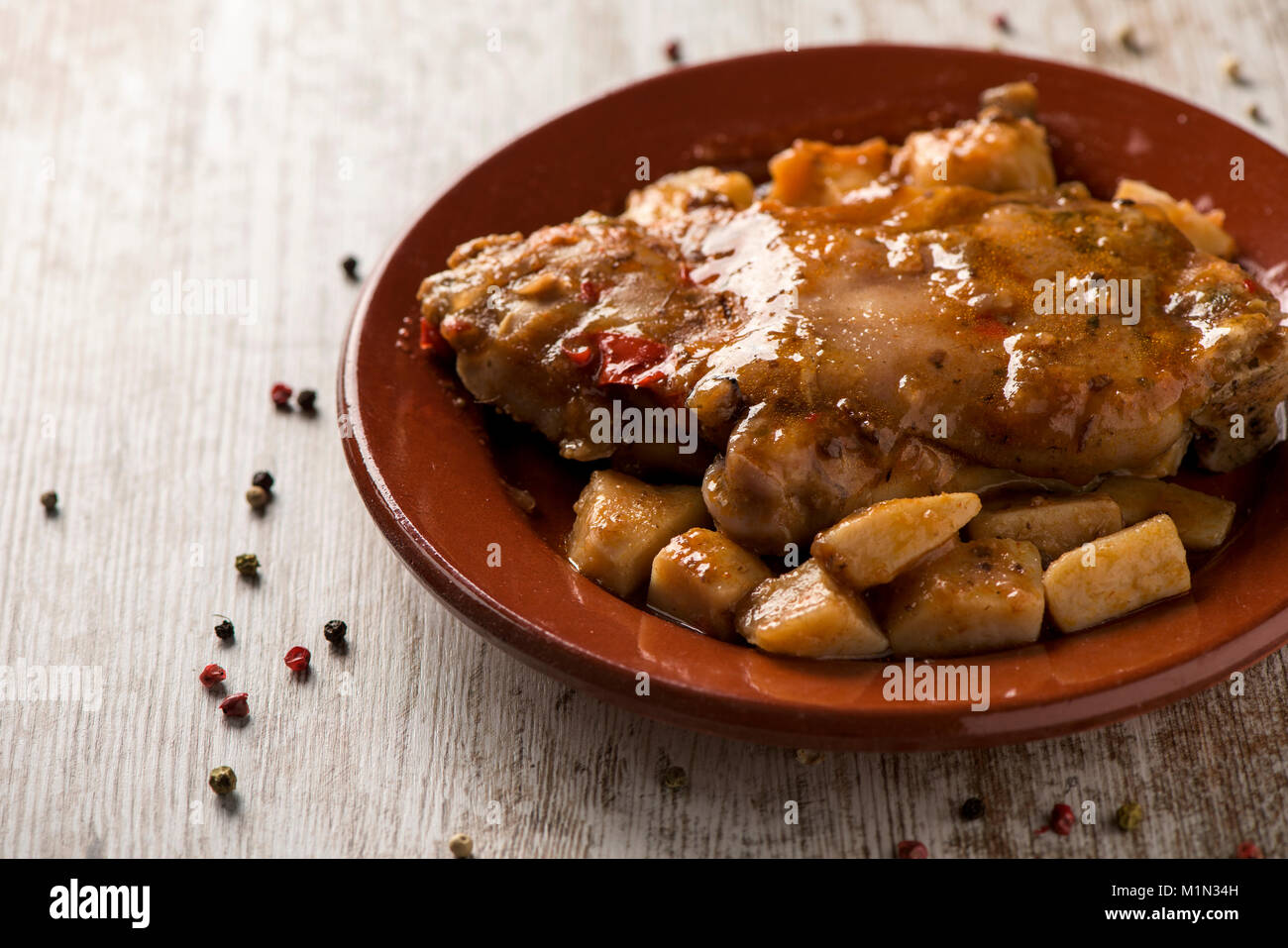 closeup of a brown earthenware plate with manitas de cerdo, spanish stewed pigs trotters, on a white rustic wooden table Stock Photo