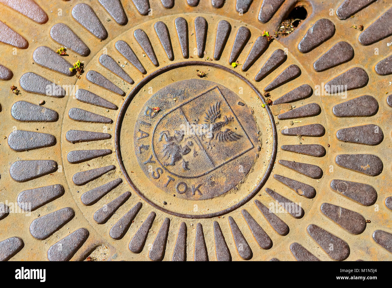 Old cast iron sewerage hatchway cover with the coat of arms of city Bialystok, Poland. Iron manhole on the road of the big city Stock Photo
