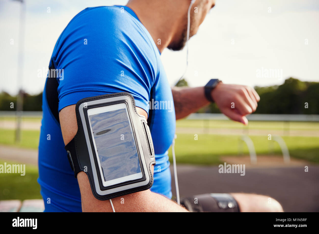 Male athlete wearing smartphone armband checking smartwatch Stock Photo