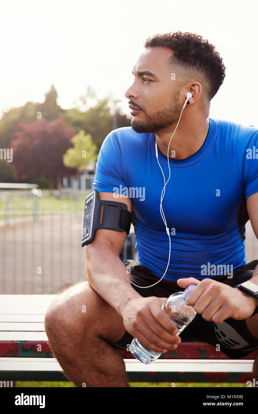 Young male athlete sitting on park bench holding water bottle Stock Photo